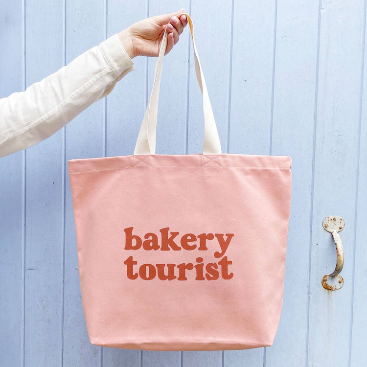 Blush Pink Tote Bag with ‘Bakery Tourist ’ text on a Blue Background