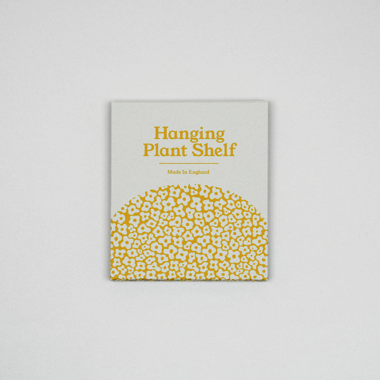 Hanging macrame plant shelf that rests nearly against the wall. Yellow and white floral print with colourful twine, brass plated hoops and crimp bars. Made in England.