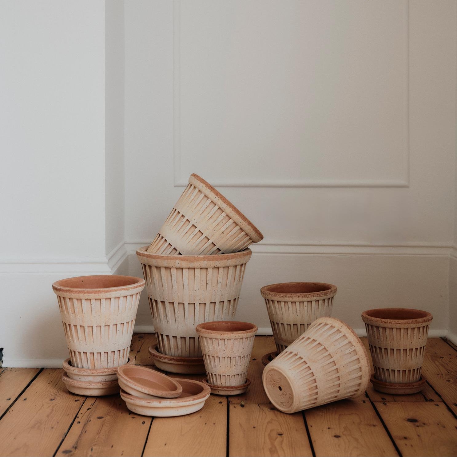Stack of bergs potter pots on a wooden floor against a white wall