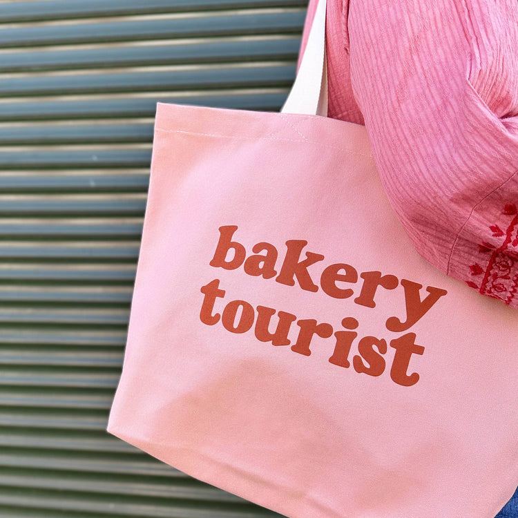 Blush Pink Tote Bag with ‘Bakery Tourist ’ text on a Green Background