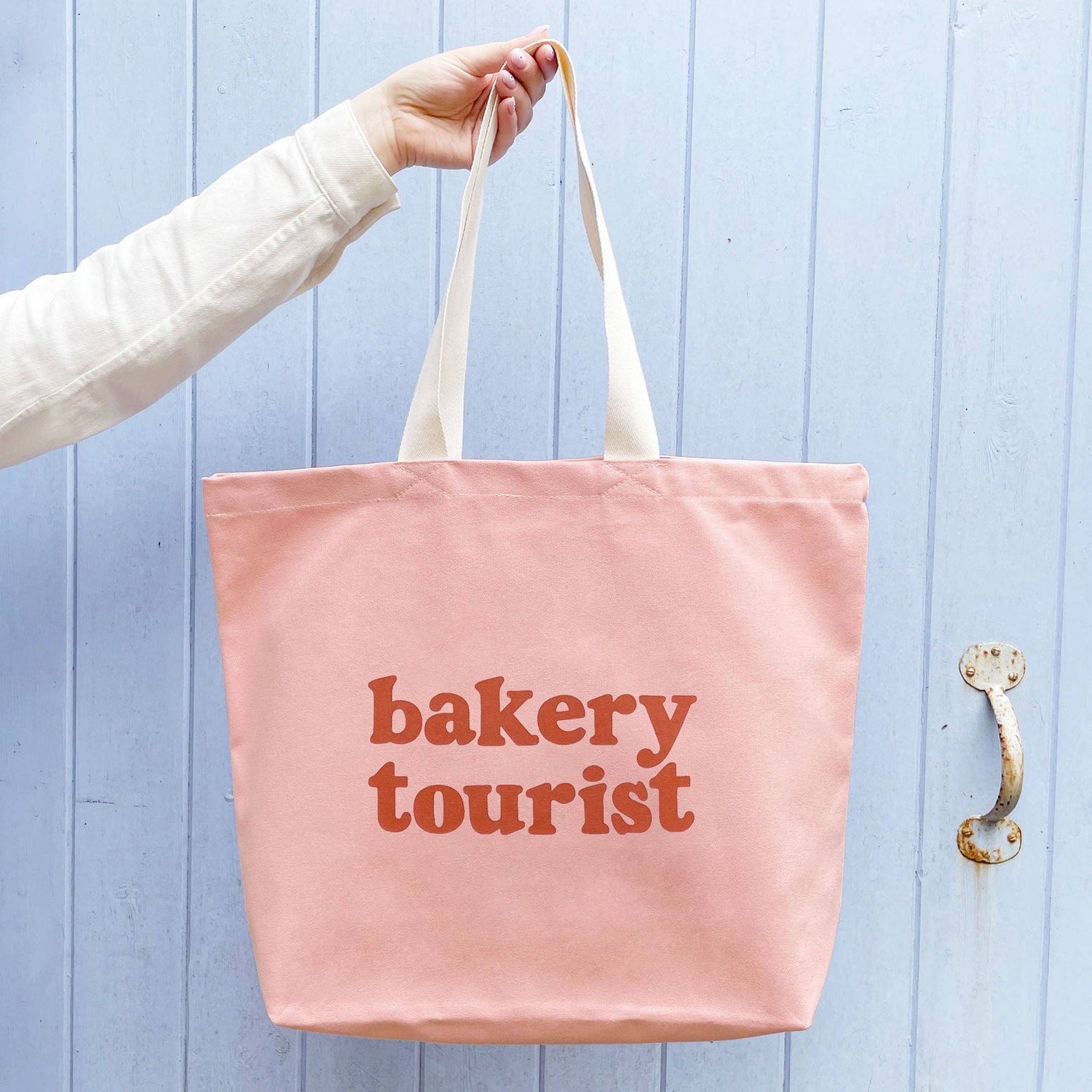 Blush Pink Tote Bag with ‘Bakery Tourist ’ text on a Blue Background
