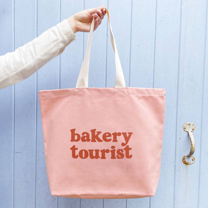 Blush Pink Tote Bag with ‘Bakery Tourist ’ text on a Blue Background