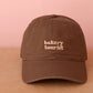 Cocoa Cotton Baseball Cap with ‘Bakery Tourist’ Text on a Neutral Background