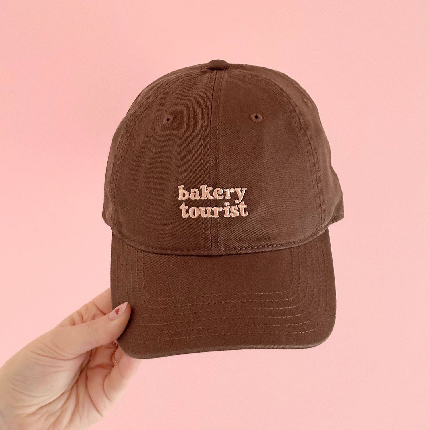 Cocoa Cotton Baseball Cap with ‘Bakery Tourist’ Text on a Pink Background