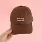 Cocoa Cotton Baseball Cap with ‘Bakery Tourist’ Text on a Pink Background