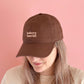 Person Wearing a Cocoa Cotton Baseball Cap with ‘Bakery Tourist’ Text on a Pink Background