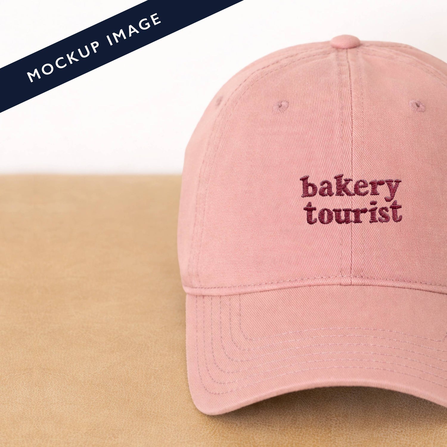 Dusty Rose Cotton Baseball Cap with ‘Bakery Tourist’ Text on a Neutral Background