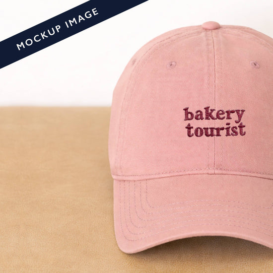 Dusty Rose Cotton Baseball Cap with ‘Bakery Tourist’ Text on a Neutral Background