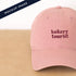 Dusty Rose Cotton Baseball Cap with ‘Bakery Tourist’ Text on a Neutral Background