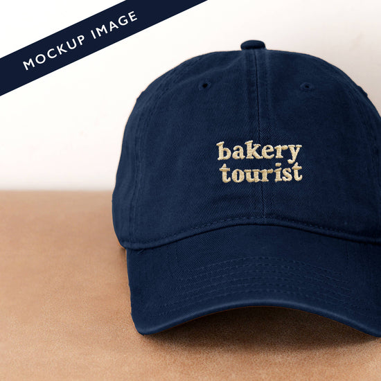 Navy Cotton Baseball Cap with ‘Bakery Tourist’ Text on a Neutral Background