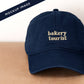 Navy Cotton Baseball Cap with ‘Bakery Tourist’ Text on a Neutral Background