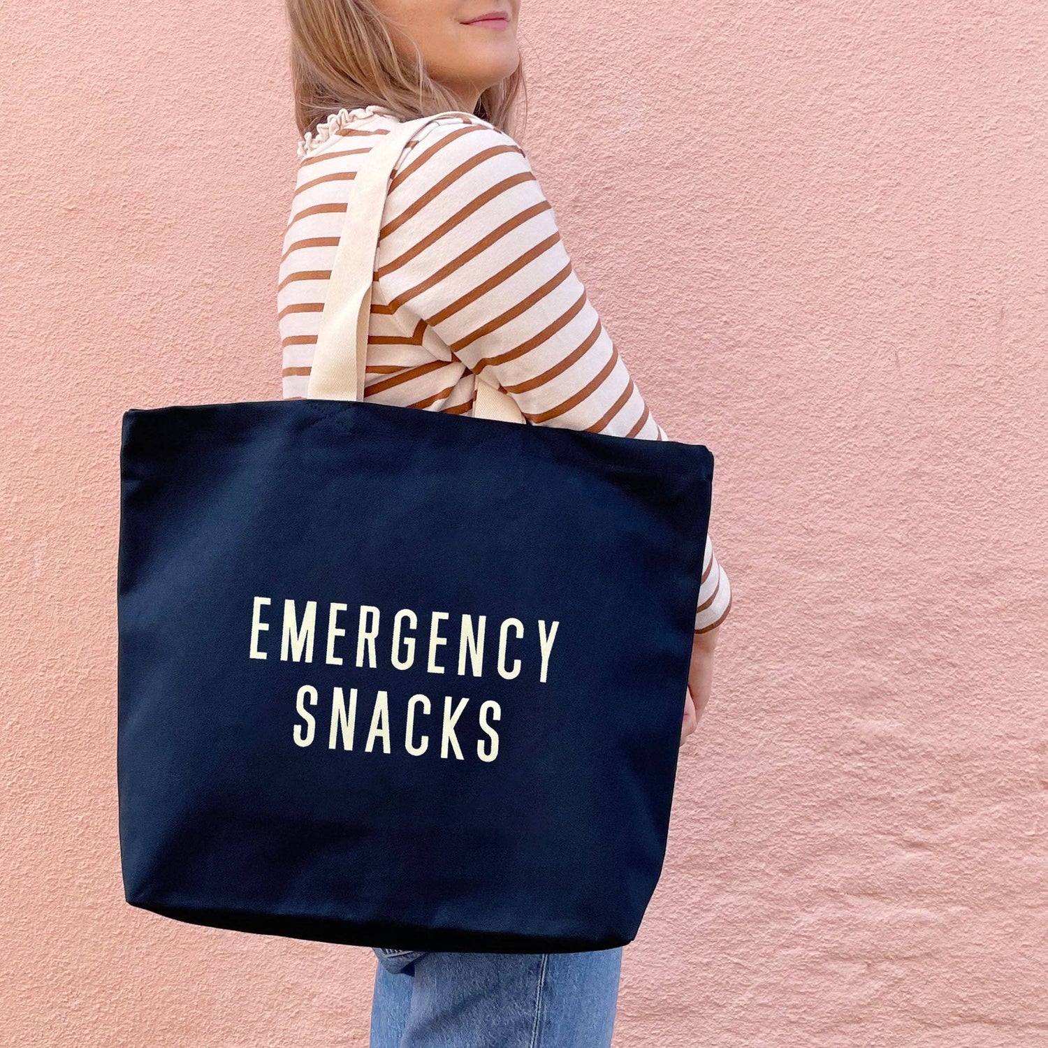 Person Wearing a Canvas Tote Bag with ‘Emergency Snacks’ Text on a Pink Background