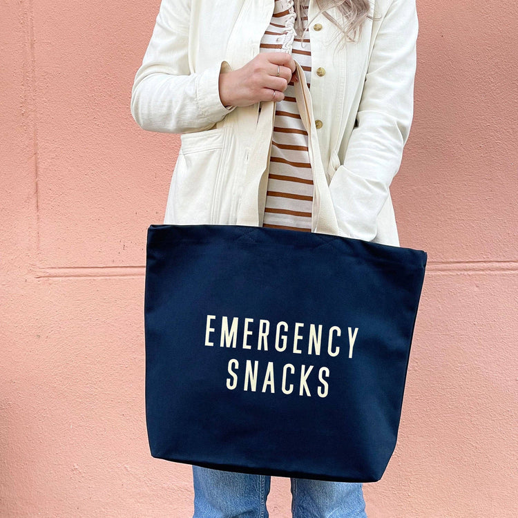 Person Wearing a Canvas Tote Bag with ‘Emergency Snacks’ Text on a Pink Background