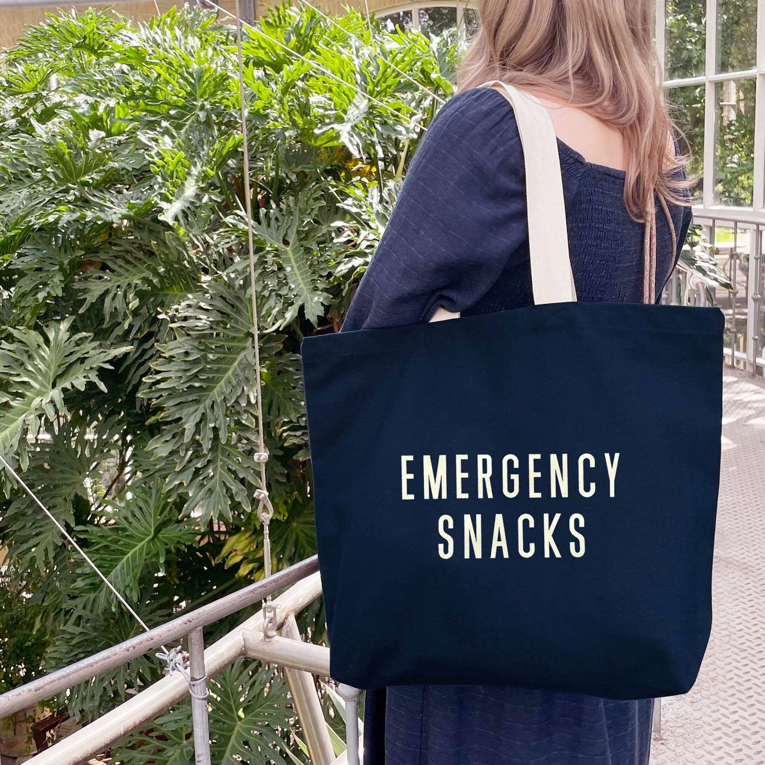 Person Wearing a Canvas Tote Bag with ‘Emergency Snacks’ Text on a Neutral Background