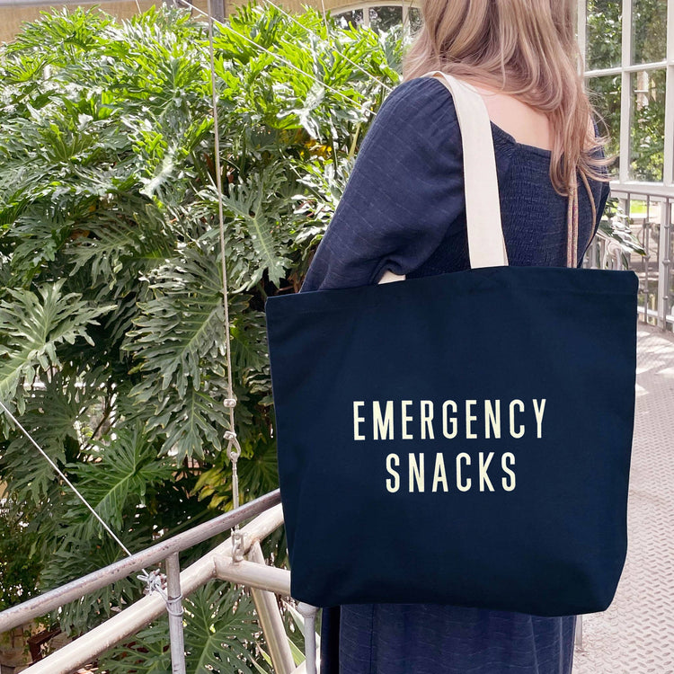 Person Wearing a Canvas Tote Bag with ‘Emergency Snacks’ Text on a Neutral Background