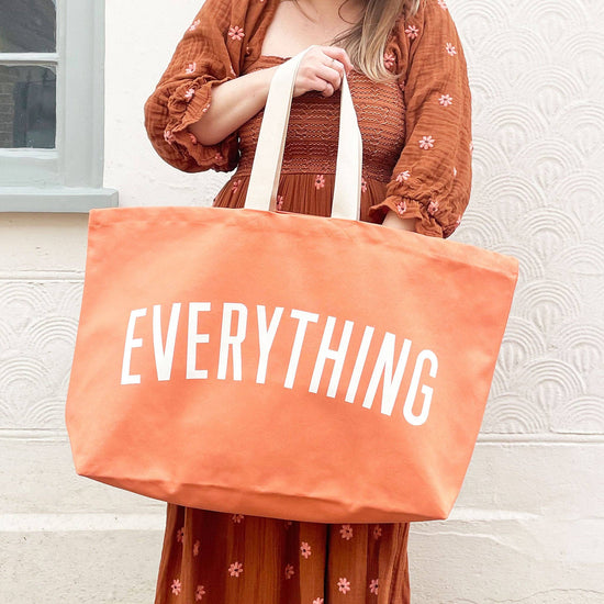Person holding an orange tote bag with &