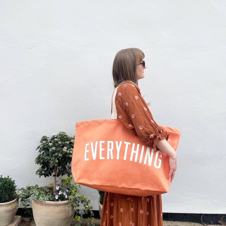 Woman holding an orange tote bag with &