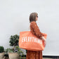 Woman holding an orange tote bag with &