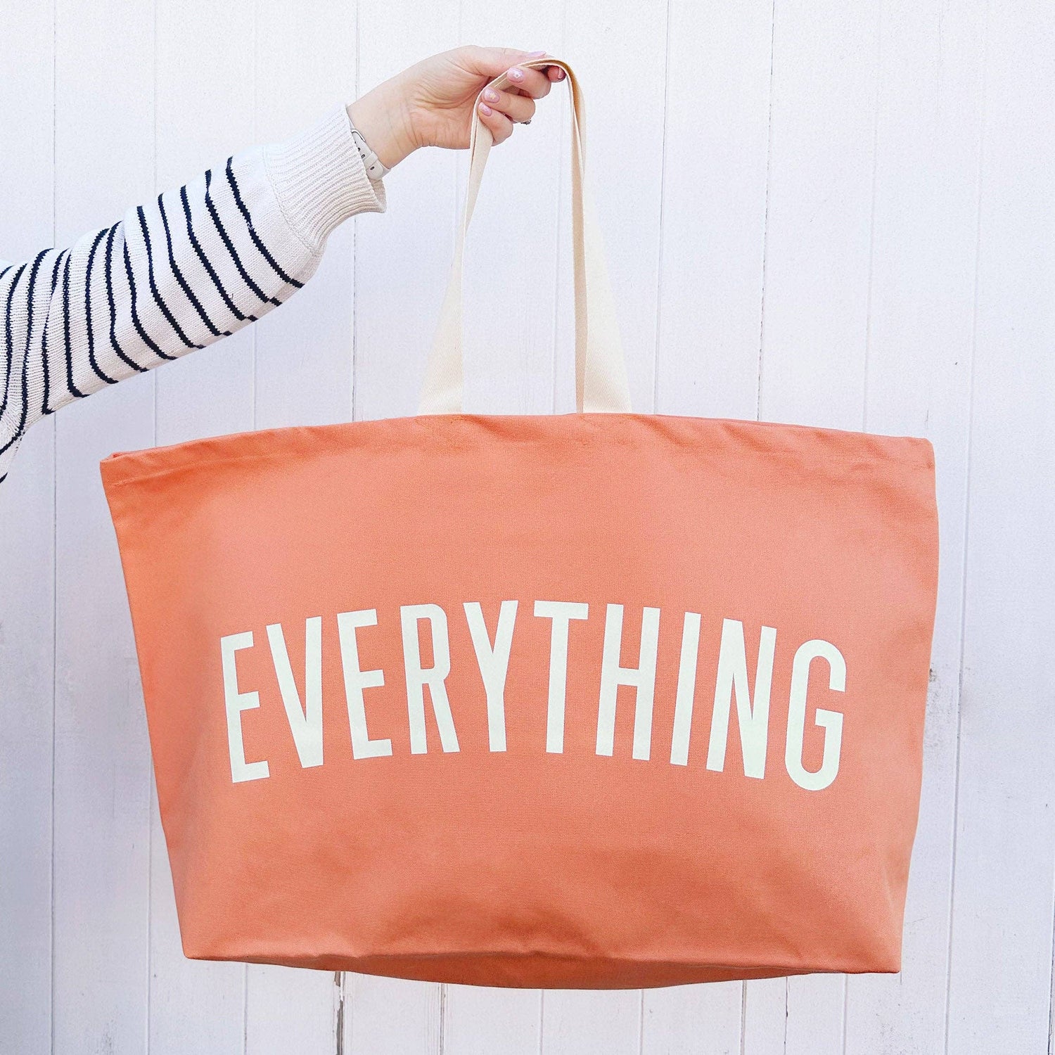 Person holding a peach-colored tote bag with &