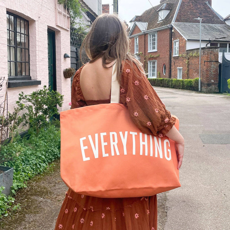 Person holding an orange tote bag with &