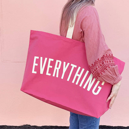 Person Carrying a Bright Pink Really Big Bag with ‘Everything’ Text on a Pink Background