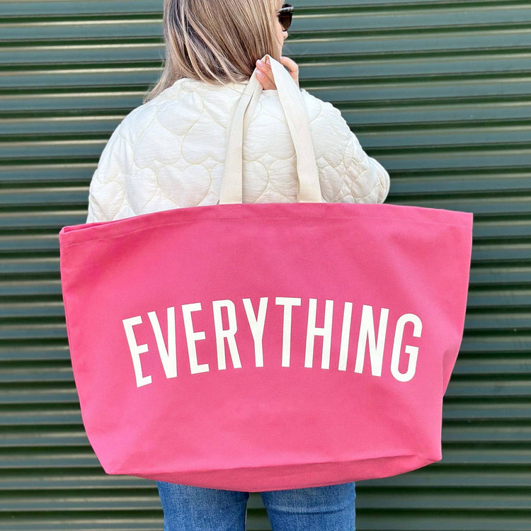 Person Carrying a Bright Pink Really Big Bag with ‘Everything’ Text on a Green Background