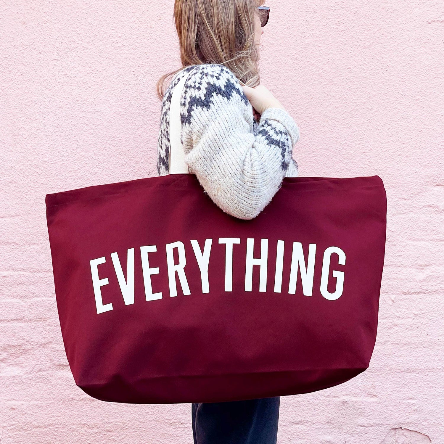 Person Carrying a Burgundy Really Big Bag with ‘Everything’ Text on a Pink Background