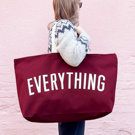 Person Carrying a Burgundy Really Big Bag with ‘Everything’ Text on a Pink Background
