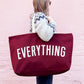 Person Carrying a Burgundy Really Big Bag with ‘Everything’ Text on a Pink Background