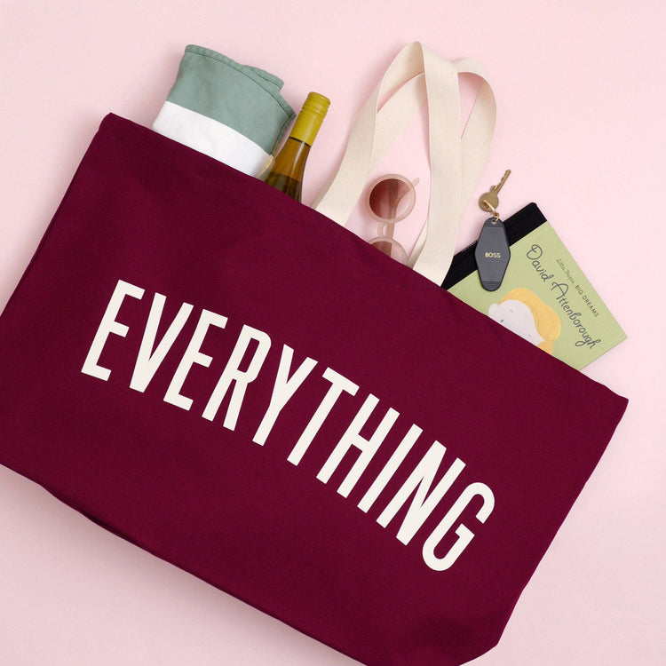 Person Carrying a Burgundy Really Big Bag with ‘Everything’ Text on a Pink Background