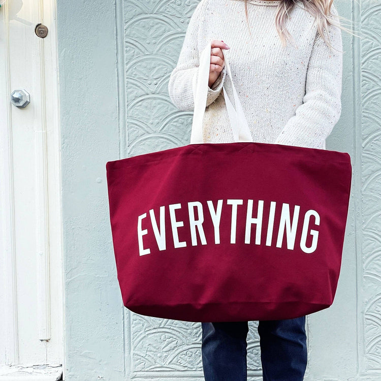 Person Carrying a Burgundy Really Big Bag with ‘Everything’ Text on a Mixed Background