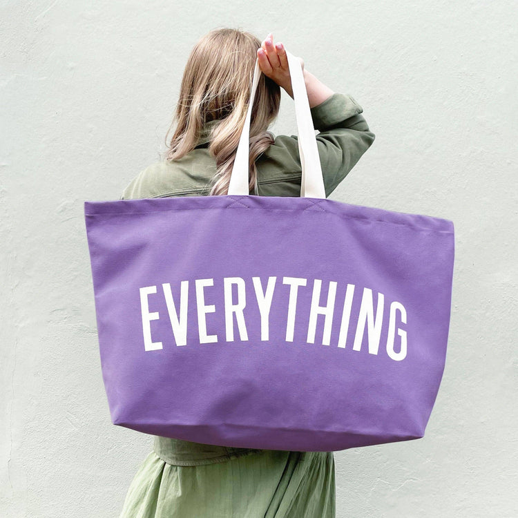 Person Carrying a Lavender Really Big Bag with ‘Everything’ Text on a White Background