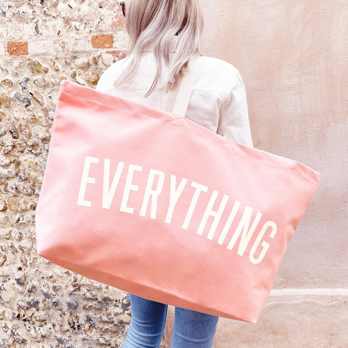 Person Carrying a Pink Really Big Bag with ‘Everything’ Text on a Neutral Background