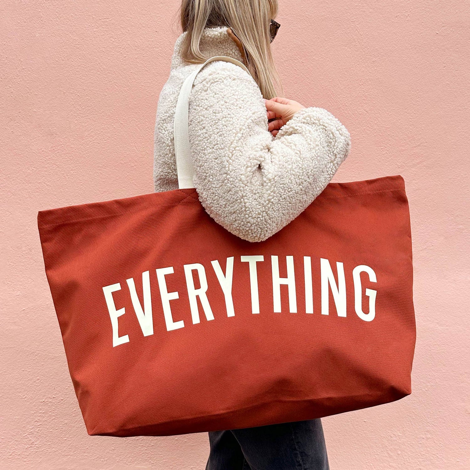 Person Carrying a Rust Really Big Bag with ‘Everything’ Text on a Pink Background