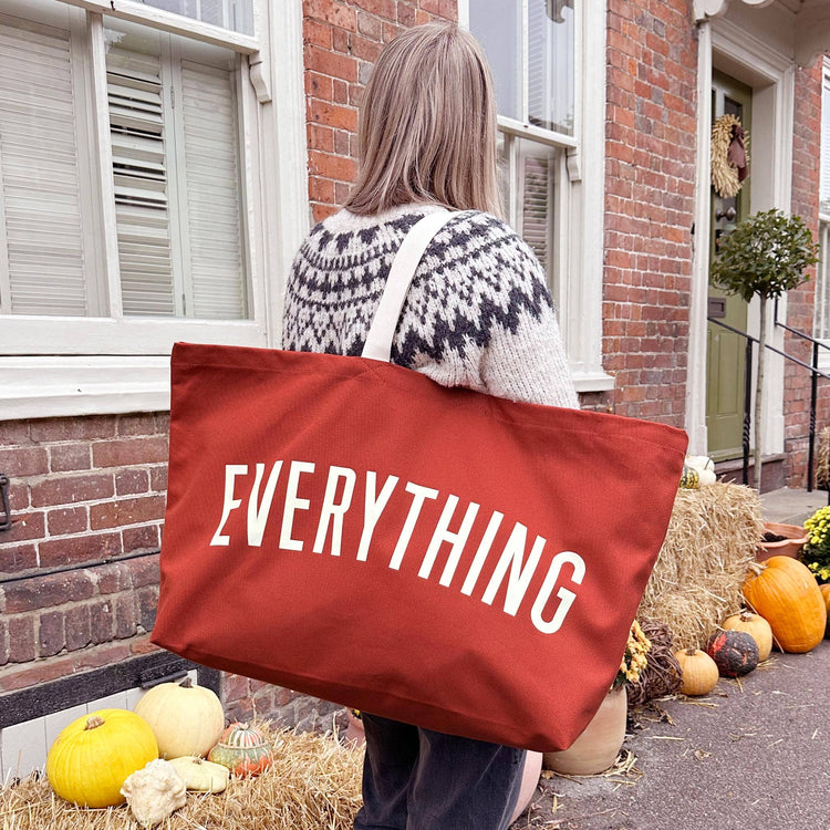 Person Carrying a Rust Really Big Bag with ‘Everything’ Text on a Halloween Background