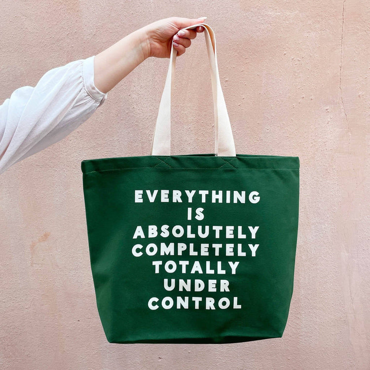 Green tote bag with motivational text held by a person against a beige background