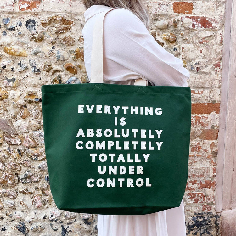 Person holding a green tote bag with text against a stone wall background