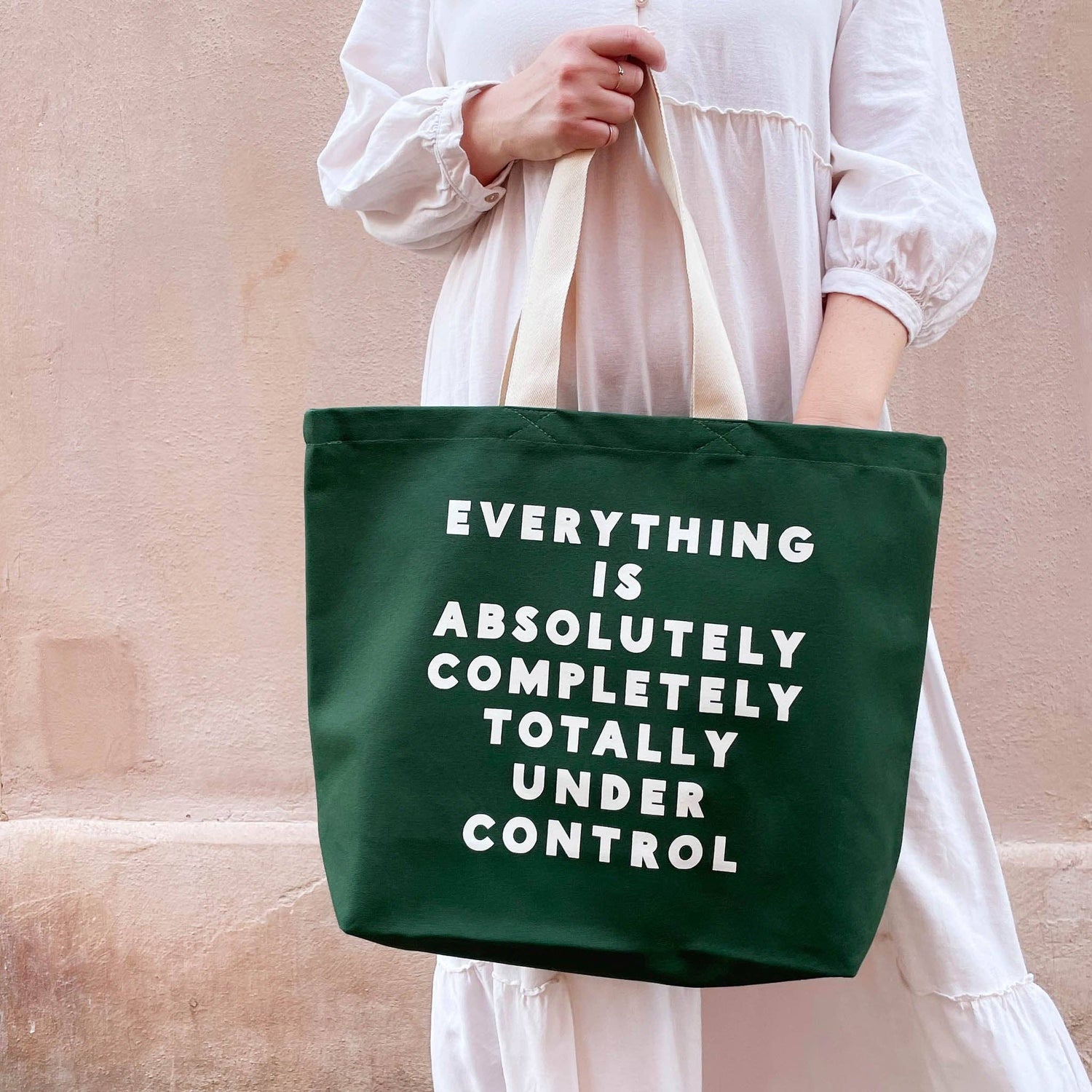 Person holding a green tote bag with text against a beige wall