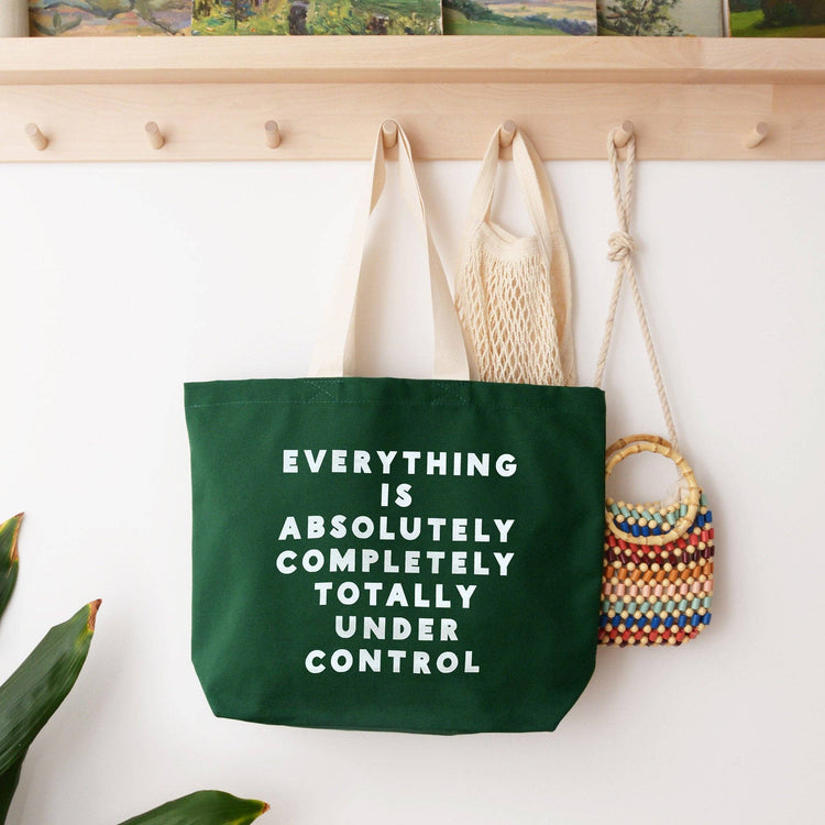 Green tote bag with motivational quote hanging on a wall with other bags.