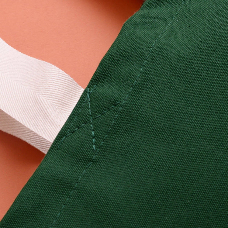 Close-up of green fabric with white stitching on a peach background