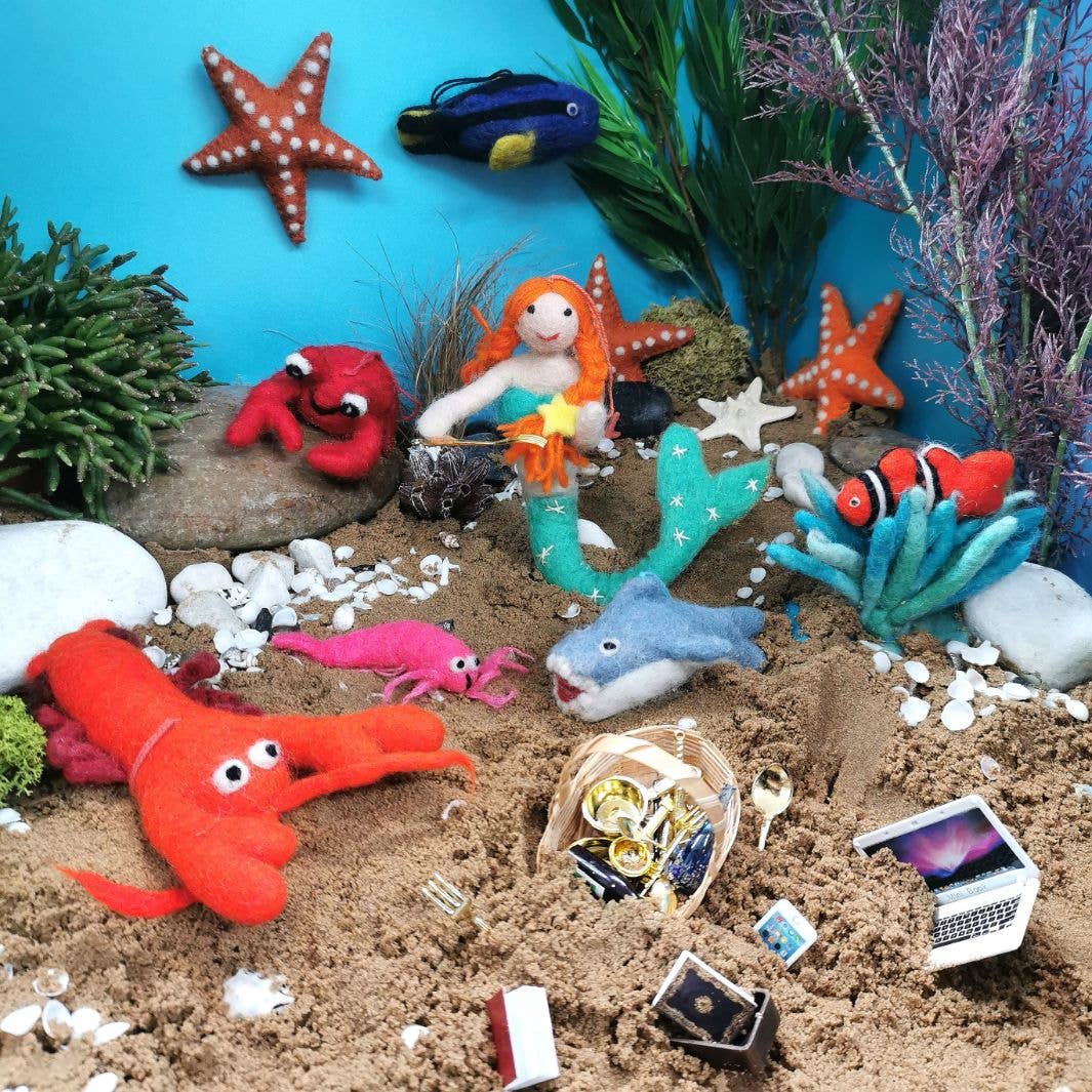 Toy scene with sea creatures and mermaid on a sandy surface with plants and blue background