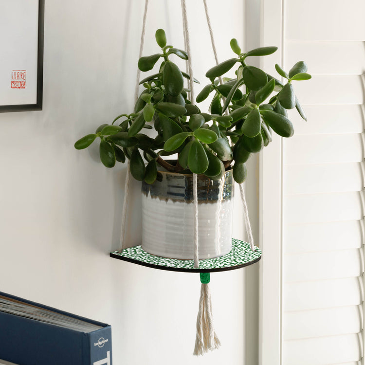 Hanging macrame plant shelf that rests nearly against the wall. ‘Forget me not’ green and white floral print with colourful twine, brass plated hoops and crimp bars. Made in England. 
