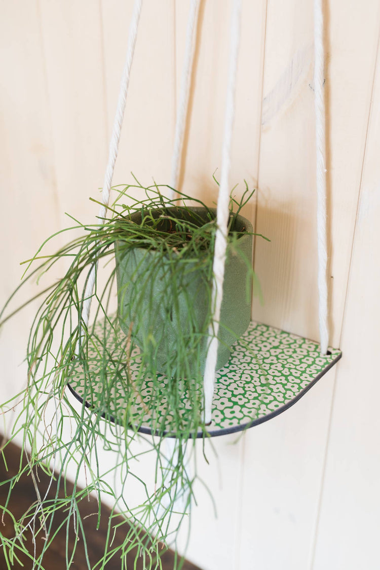 Hanging macrame plant shelf that rests nearly against the wall. ‘Forget me not’ green and white floral print with colourful twine, brass plated hoops and crimp bars. Made in England. 
