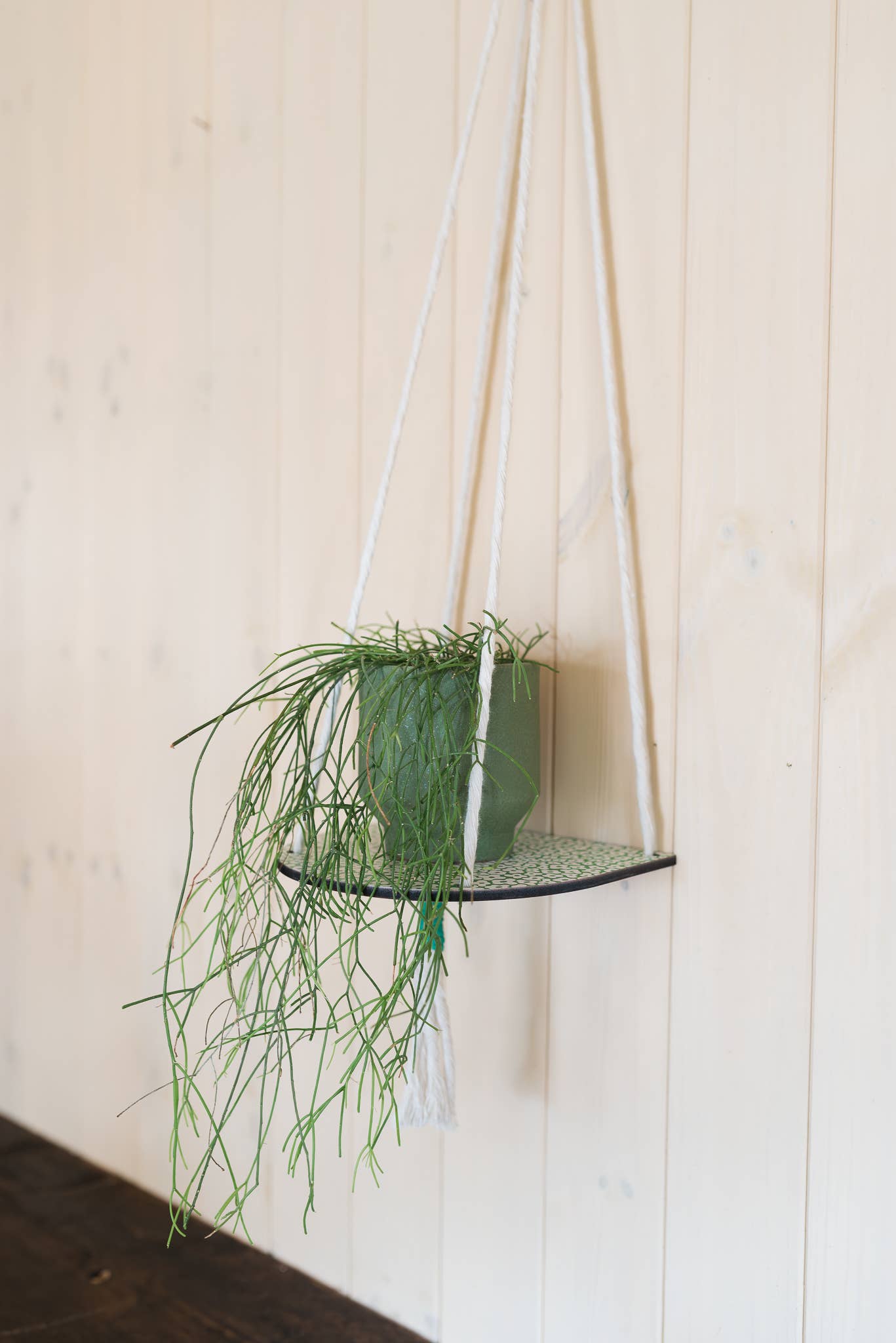 Hanging macrame plant shelf that rests nearly against the wall. ‘Forget me not’ green and white floral print with colourful twine, brass plated hoops and crimp bars. Made in England. 