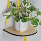 Hanging macrame plant shelf that rests nearly against the wall. Yellow and white floral print with colourful twine, brass plated hoops and crimp bars. Made in England. 