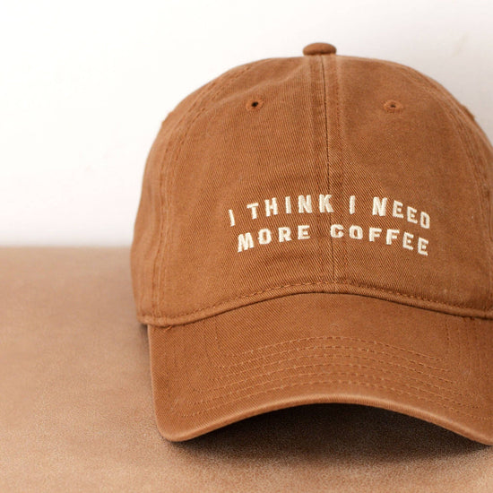 Cotton Baseball Cap with ‘I Think I Need More Coffee’ Text on a neutral Background