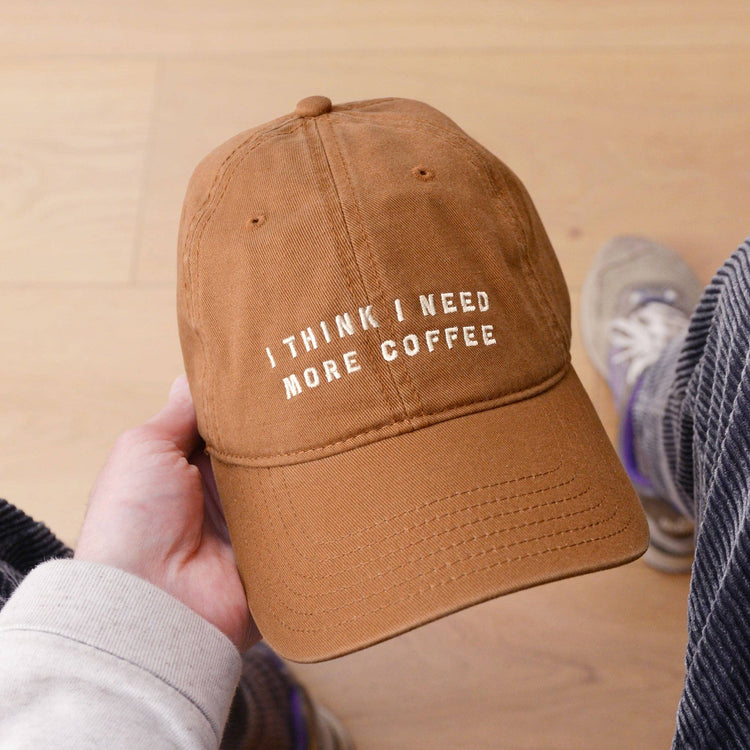 Cotton Baseball Cap with ‘I Think I Need More Coffee’ Text on a neutral Background