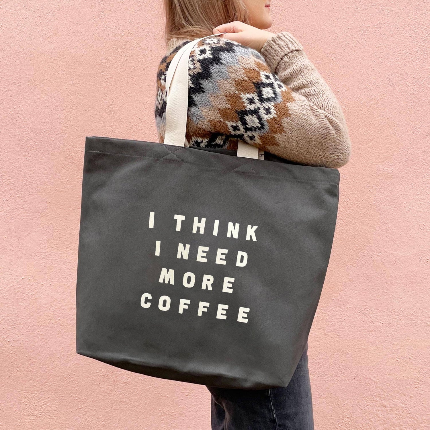 Person Carrying a Grey Tote Bag with ‘I Think I Need More Coffee’ Text on a Pink Background