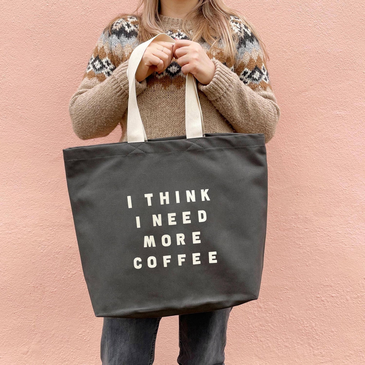 Person Carrying a Grey Tote Bag with ‘I Think I Need More Coffee’ Text on a Pink Background