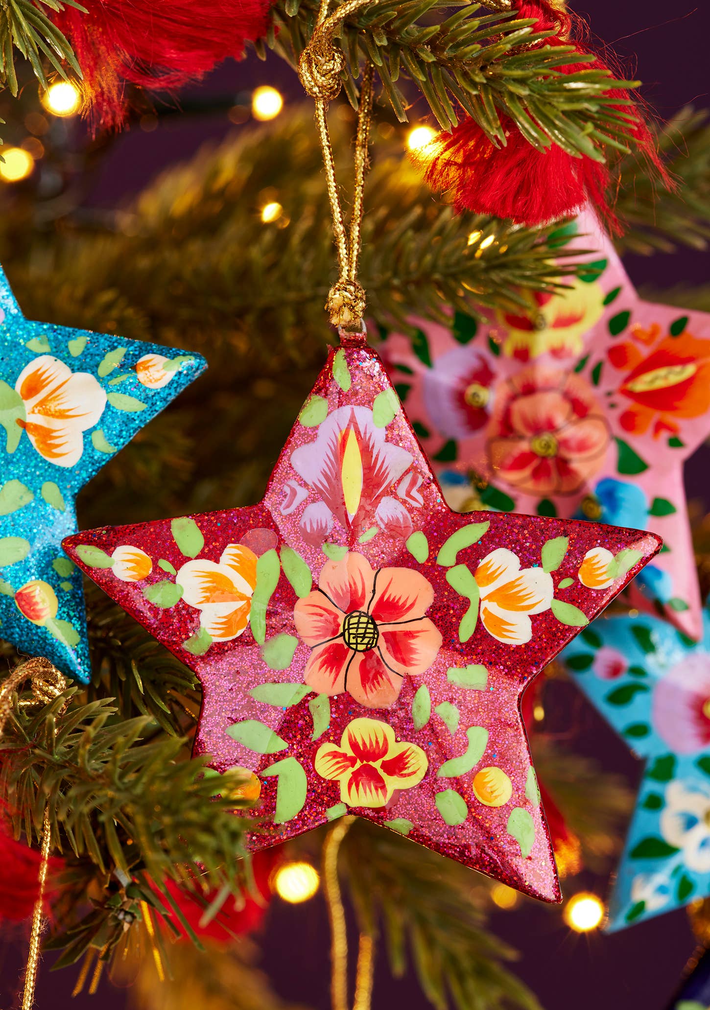 Decorative star ornaments with floral patterns hanging on a Christmas tree.